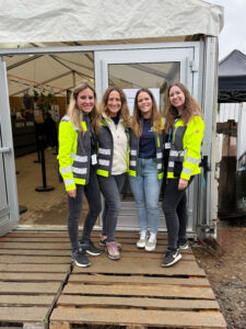Vier lächelnde Spektralwerk-Mitarbeiterinnen in gelben Warnwesten vor dem Personalbüro der Nature One.