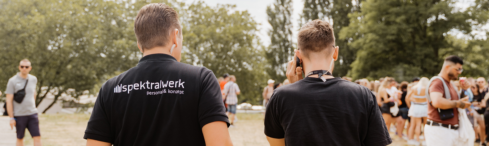 Zwei Männer in schwarzen Polo-T-Shirts gehen nebeneinander her. Sie tragen beide Funkgeräte mit Kabeln im Ohr.