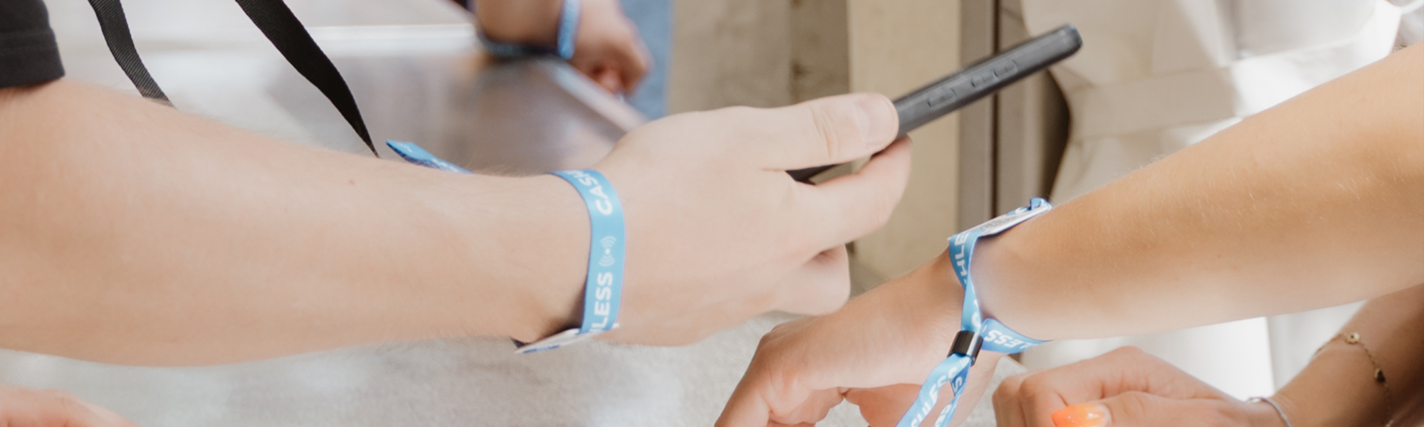 Eine Hand mit Smartphone scannt den Chip des Festivalbändchens an einer anderen Hand.